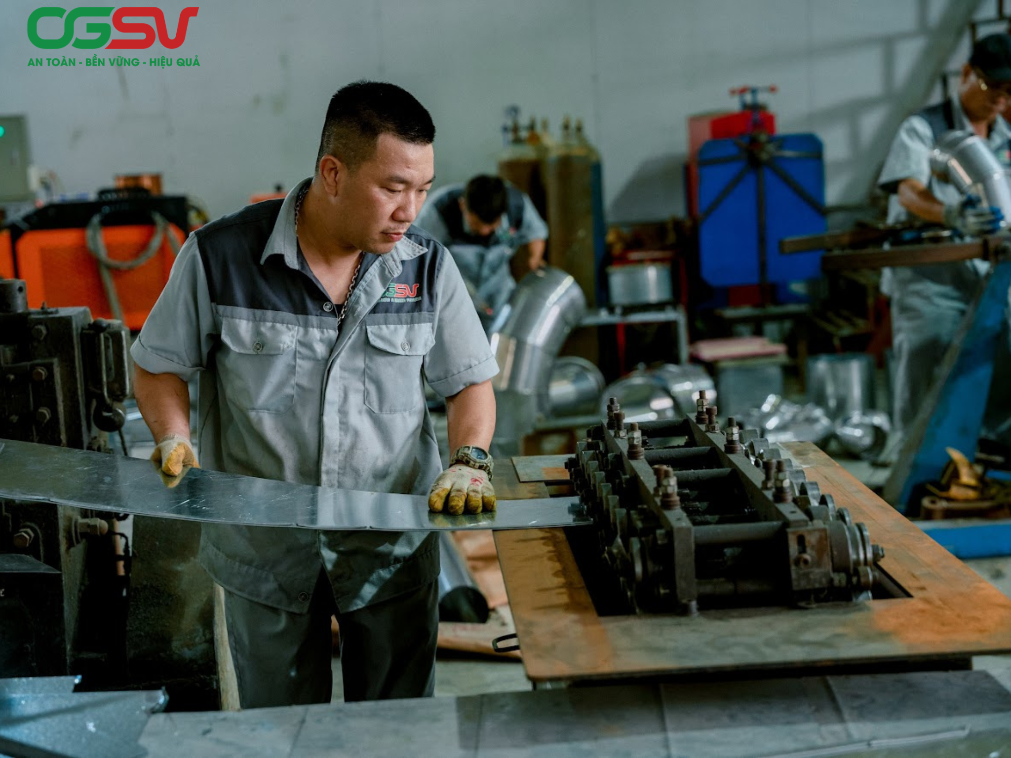 Công nhân gia công tấm kim loại bằng máy cán trong xưởng sản xuất ống gió phục vụ hệ thống thông gió và điều hòa không khí.